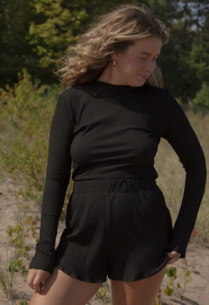 Front view of a straight size model in the Black Rib Cropped Long Sleeve Top, standing outside on grassy sand.