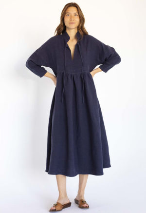 woman wearing navy oversized dress with dolman sleeves and gathered midi skirt with collar and ties at neck