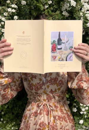 woman holding yellow book in front of bushes of white flowers