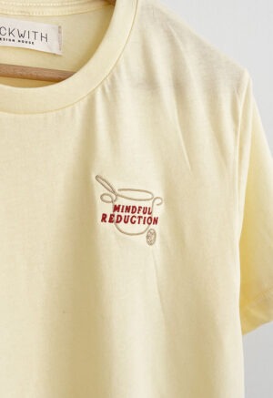 yellow t-shirt hanging on hanger with embroidered text