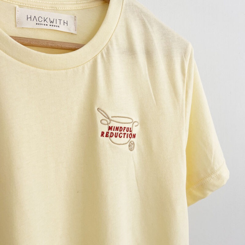 yellow t-shirt hanging on hanger with embroidered text