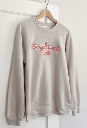 cream sweatshirt hanging on hanger with red embroidery writing