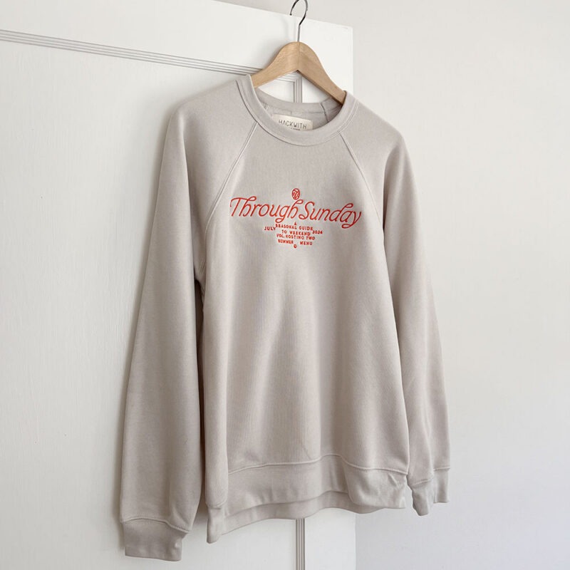 cream sweatshirt hanging on hanger with red embroidery writing