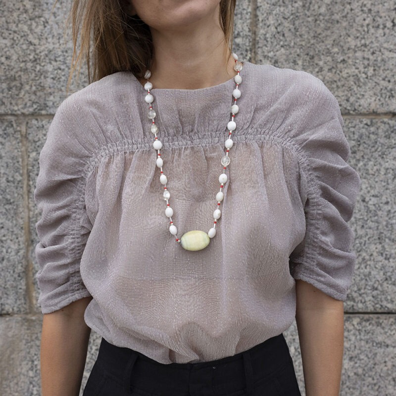 woman in grey shirt and extra long white, red and rock necklace