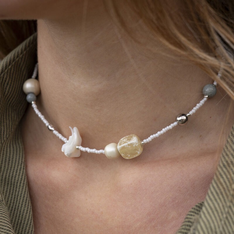 woman in green button-up with white beaded shell and stone necklace