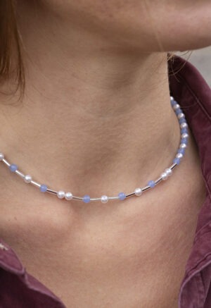 woman in maroon button-up and light blue and pearl necklace