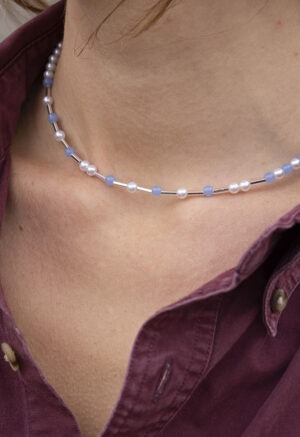 woman in maroon button-up and light blue and pearl necklace