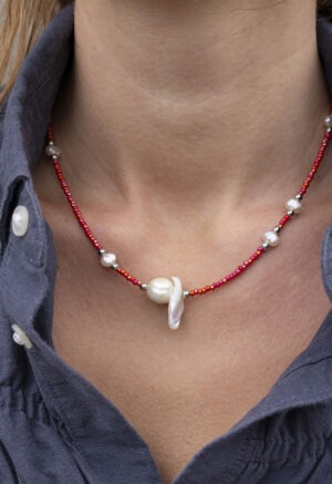 woman in dark grey button-up with red and pearl necklace