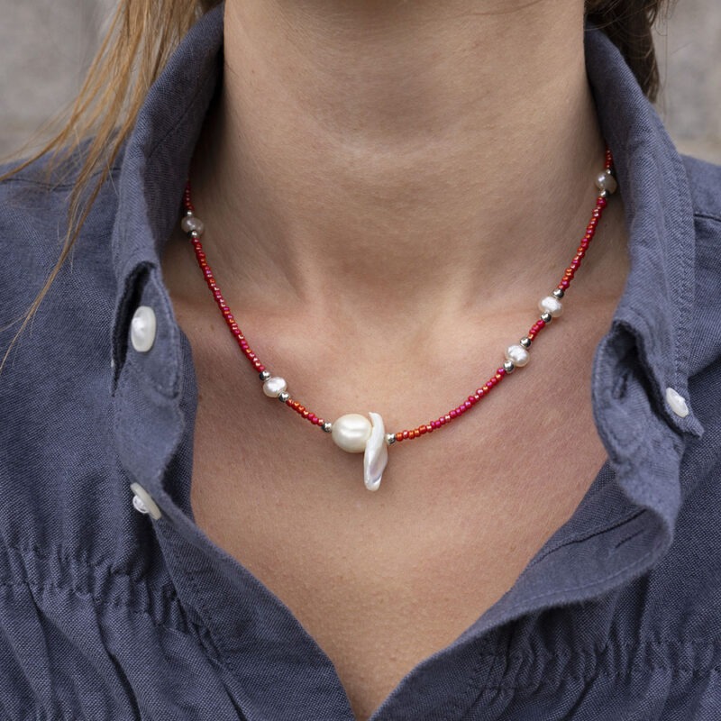 woman in dark grey button-up with red and pearl necklace