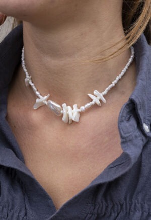 Woman in grey button-up with pearl and shell necklace