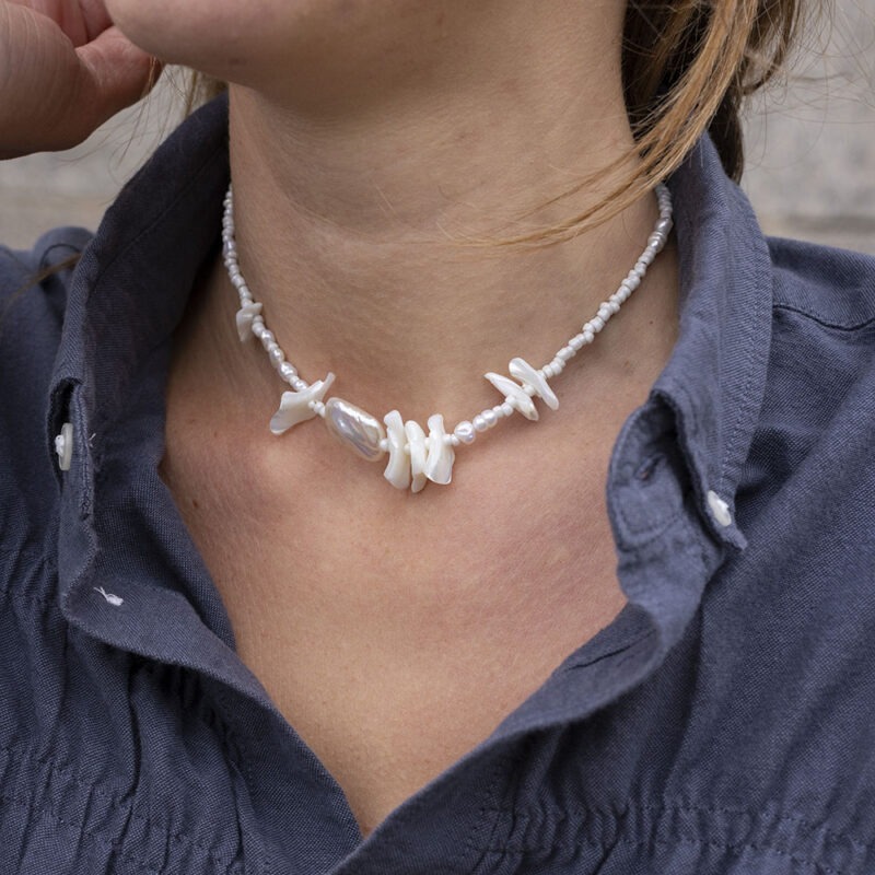 Woman in grey button-up with pearl and shell necklace