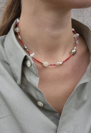 woman in grey button-up and small red beaded necklace with pearls and shells