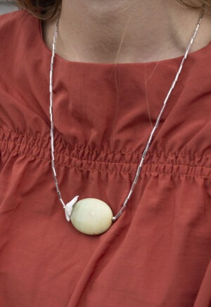 woman in burnt orange top and long silver and rock necklace.