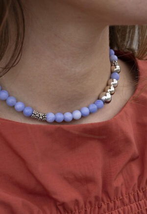 woman in burnt orange top and blue and silver beaded necklace.