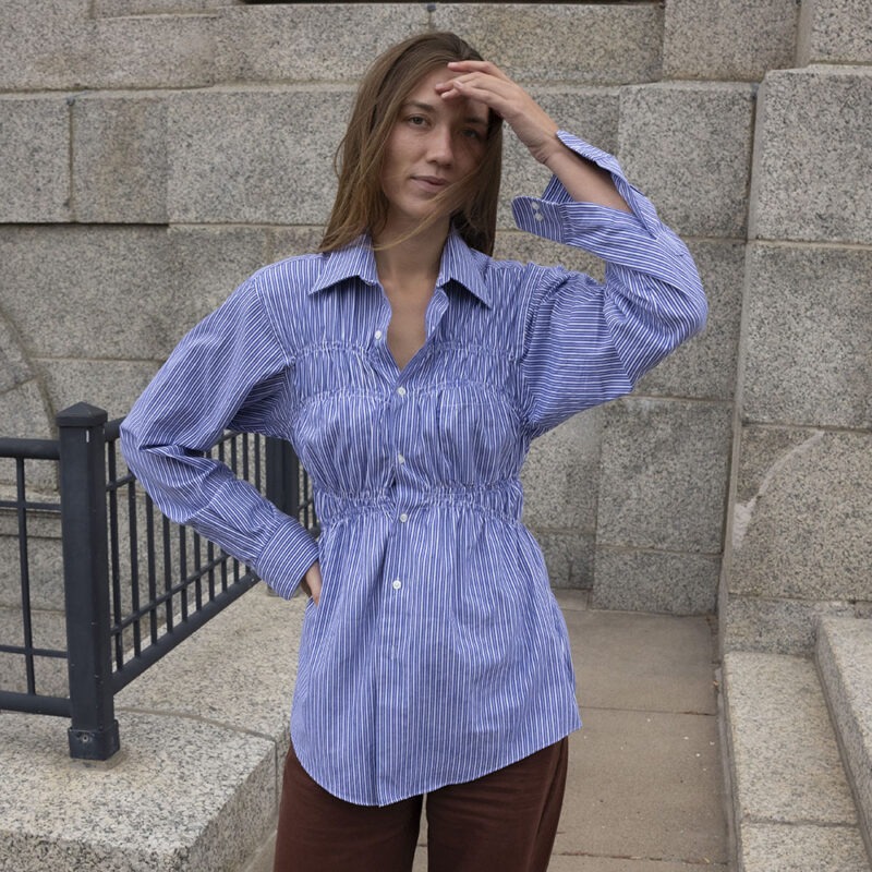 woman in blue and white stripe button-up and brown pants